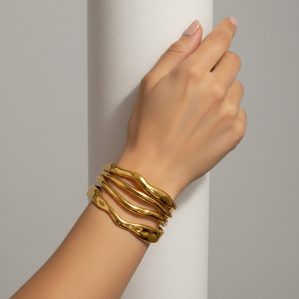 Lyza Jewels, LLC gold-toned 18k stainless steel triple wave bangle with a polished, sculptural design on a wrist.